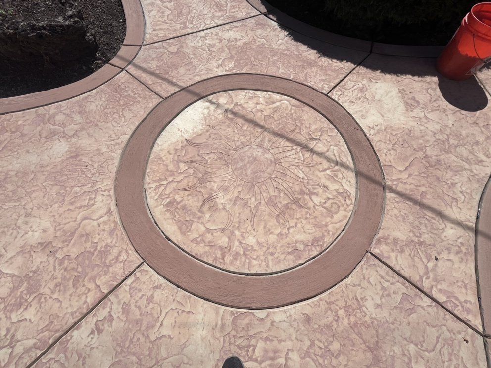 Decorative concrete patio with circular design and textured surface; brown and tan colors.