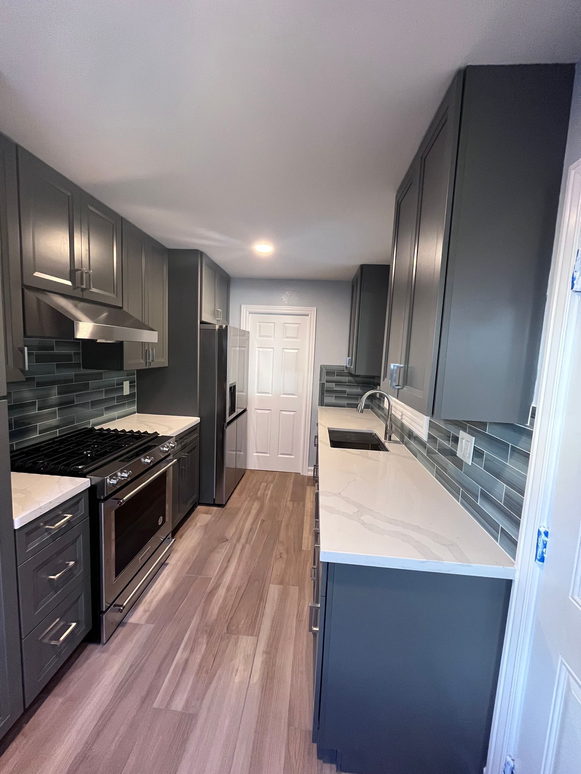 Gray kitchen with light countertops, stainless steel appliances, and wood-look flooring.