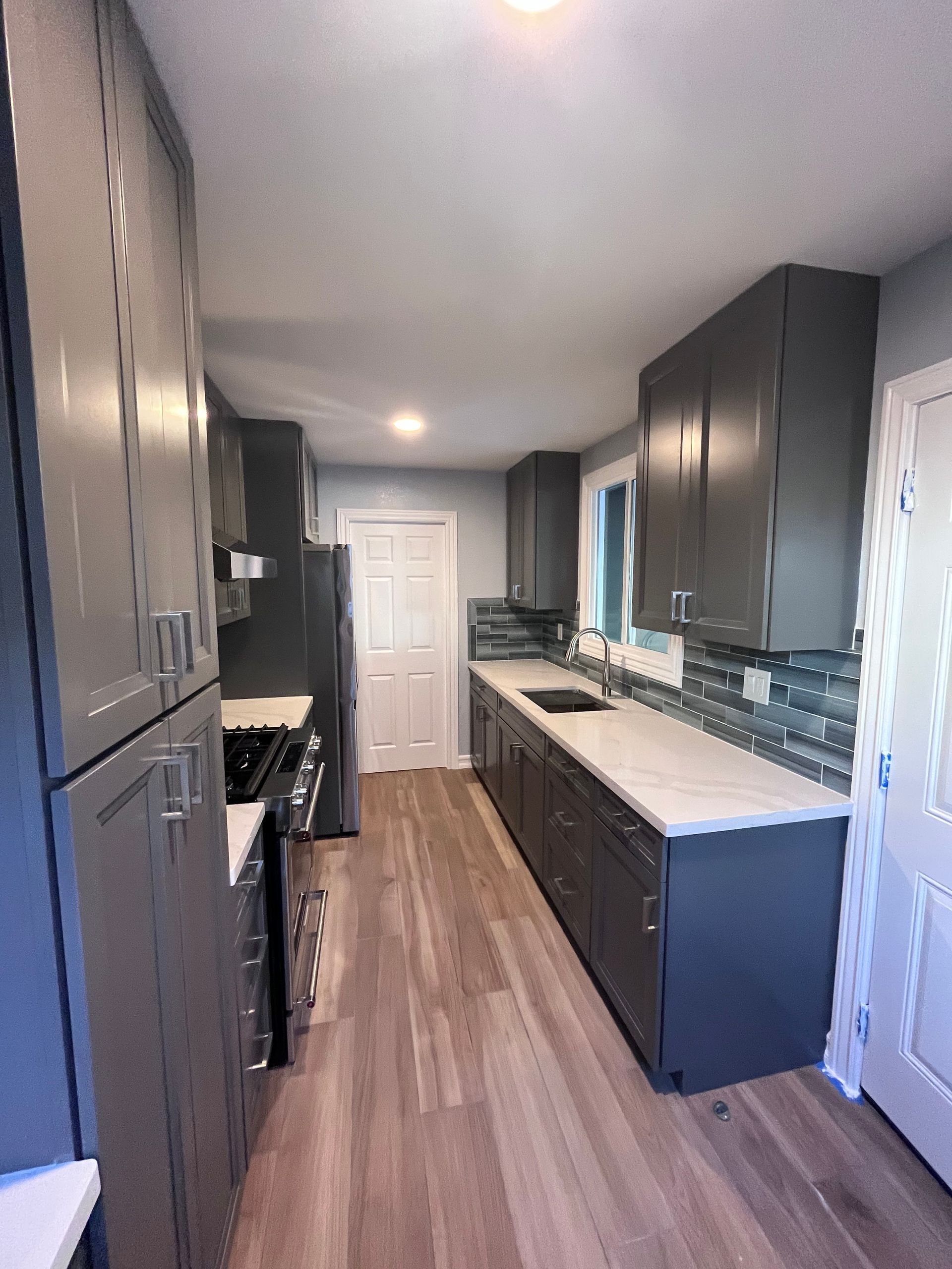Gray kitchen with cabinets, countertops, and appliances, wood-look floor, and a door at the end.