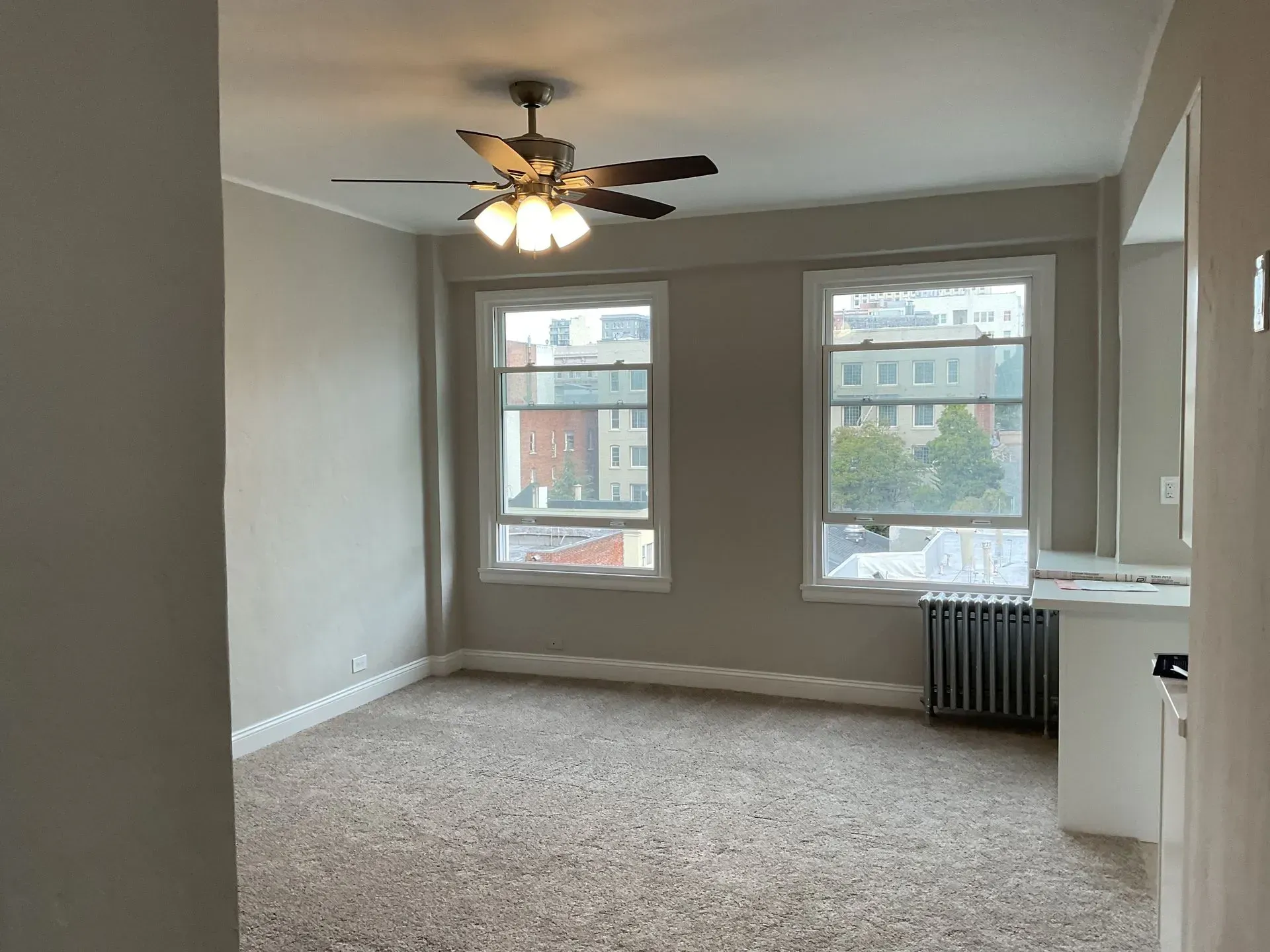 Empty room with two windows, a ceiling fan, radiator, and carpeted floor.