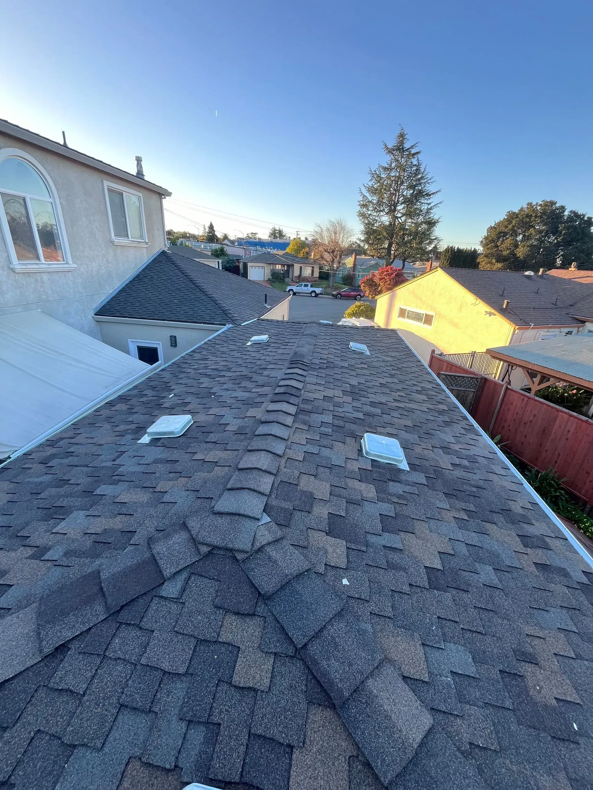 View of a shingled roof with skylights, surrounded by houses under a clear blue sky.