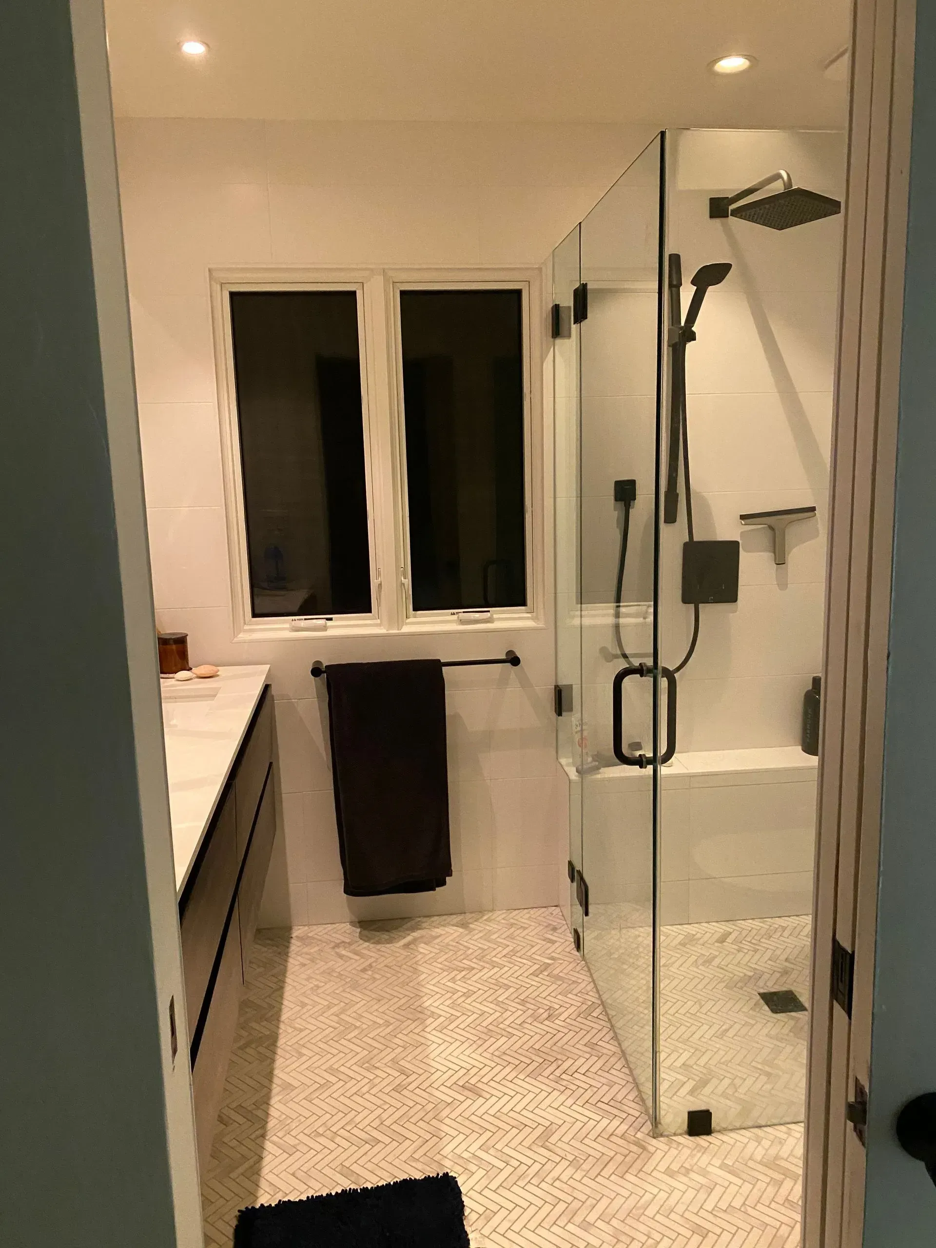 Modern bathroom with glass shower, white tile, black fixtures, and a window.