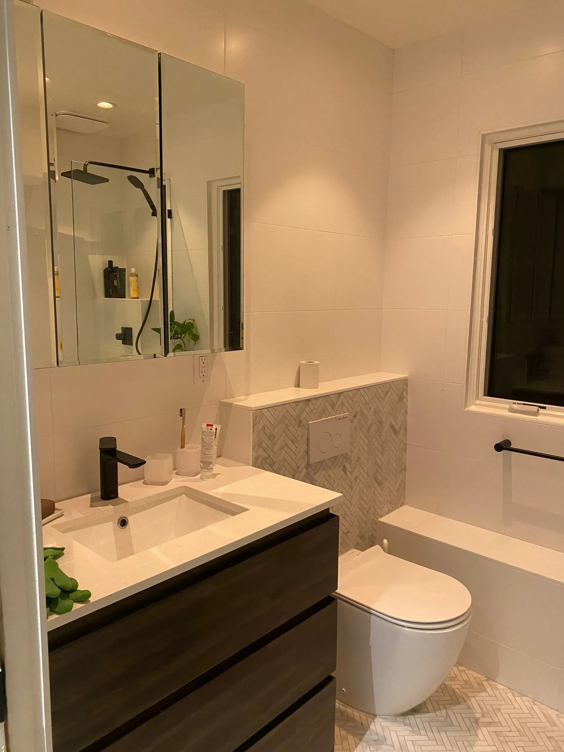 Modern bathroom with white and brown tones. Features a toilet, vanity with black faucet, and mirrored cabinet.