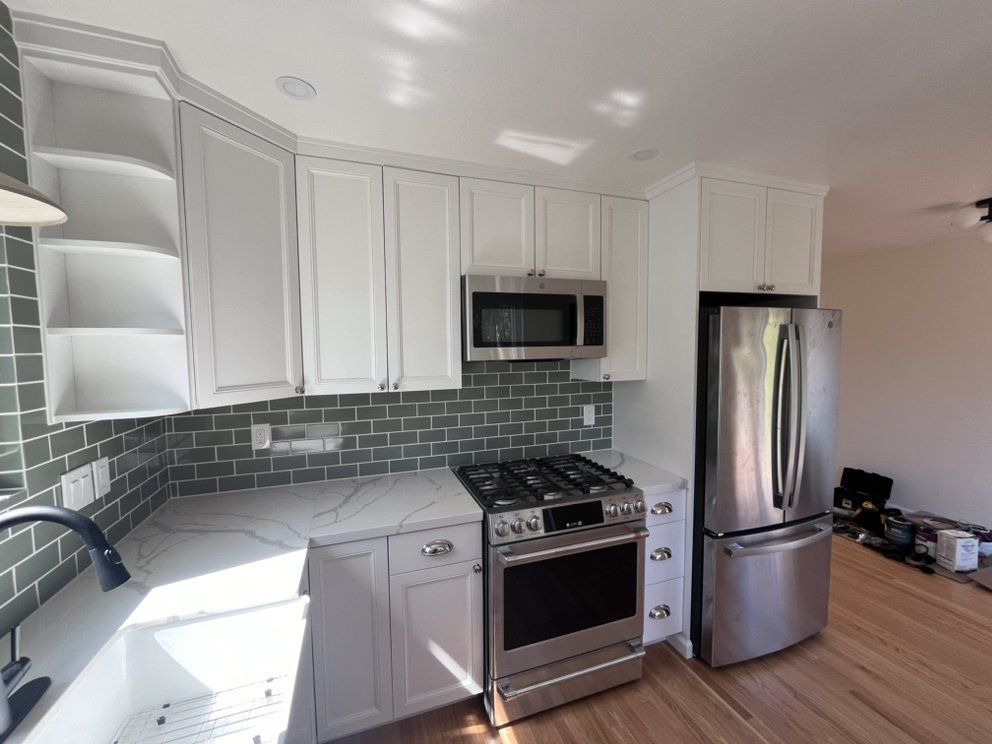 White kitchen with stainless steel appliances, green tile backsplash, and light wood flooring.