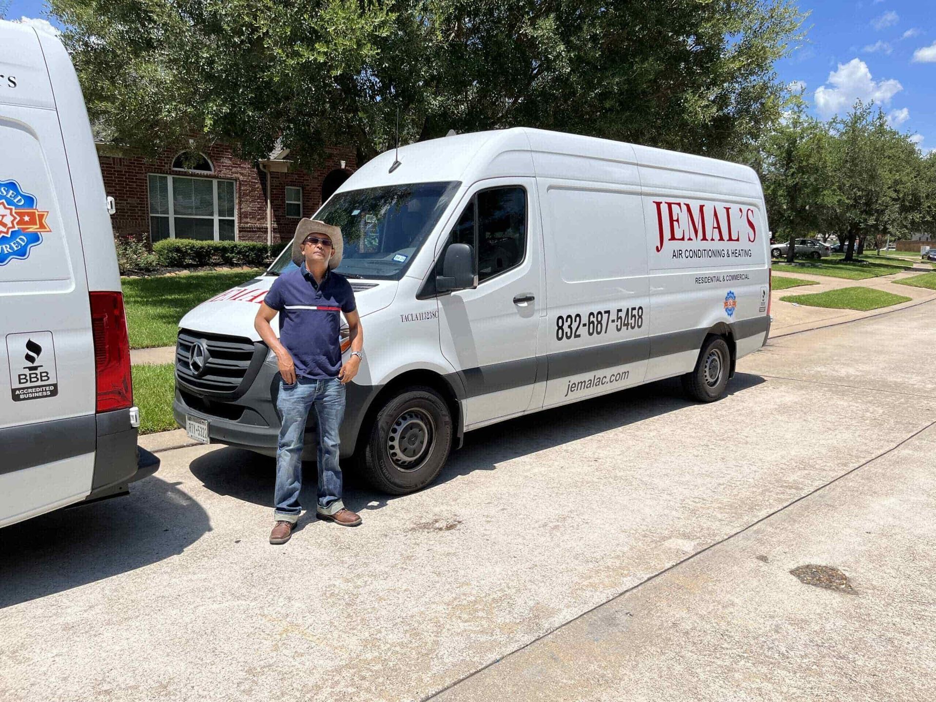 Man standing beside a white service van on a suburban street, with another van partly visible nearby.