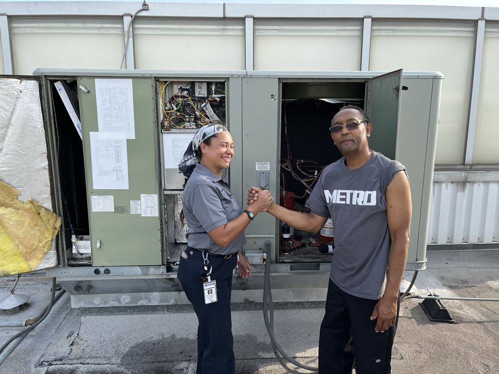 Two people shaking hands in front of an open industrial electrical cabinet on a rooftop.