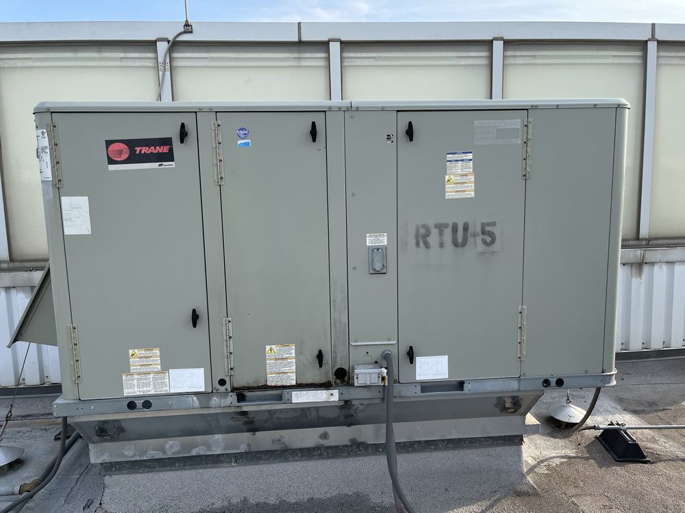 Gray rooftop HVAC unit labeled RTU-5 with ducts and cables on a flat roof