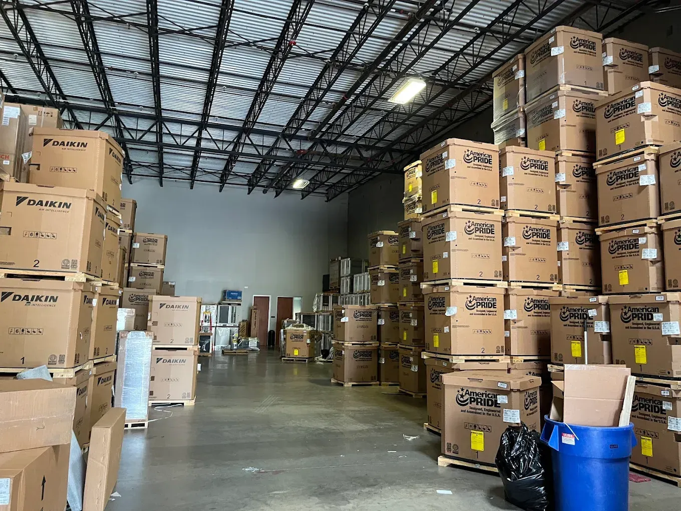 Warehouse aisle stacked with cardboard boxes and pallets under a high metal roof