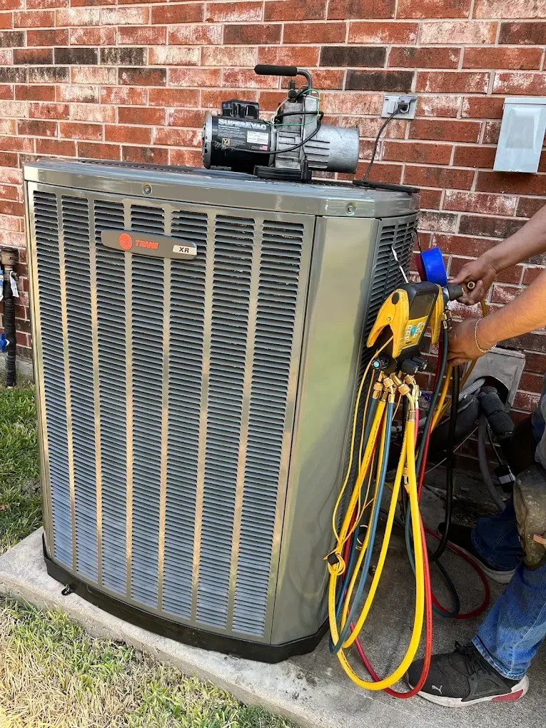 Outdoor HVAC unit with gauges and hoses attached beside a brick wall