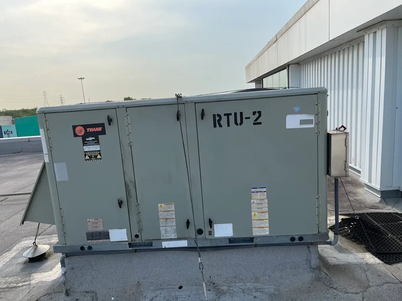 Gray rooftop HVAC unit labeled “RTU-2” beside a building, in an industrial parking lot