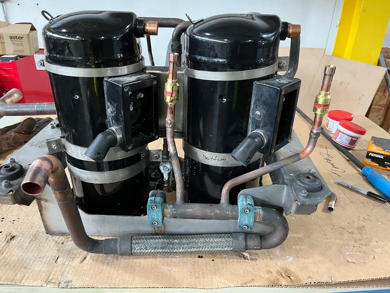 Two black compressor units mounted on a metal frame on a workshop bench