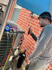 Technician checking HVAC gauges beside a brick wall under a blue canopy