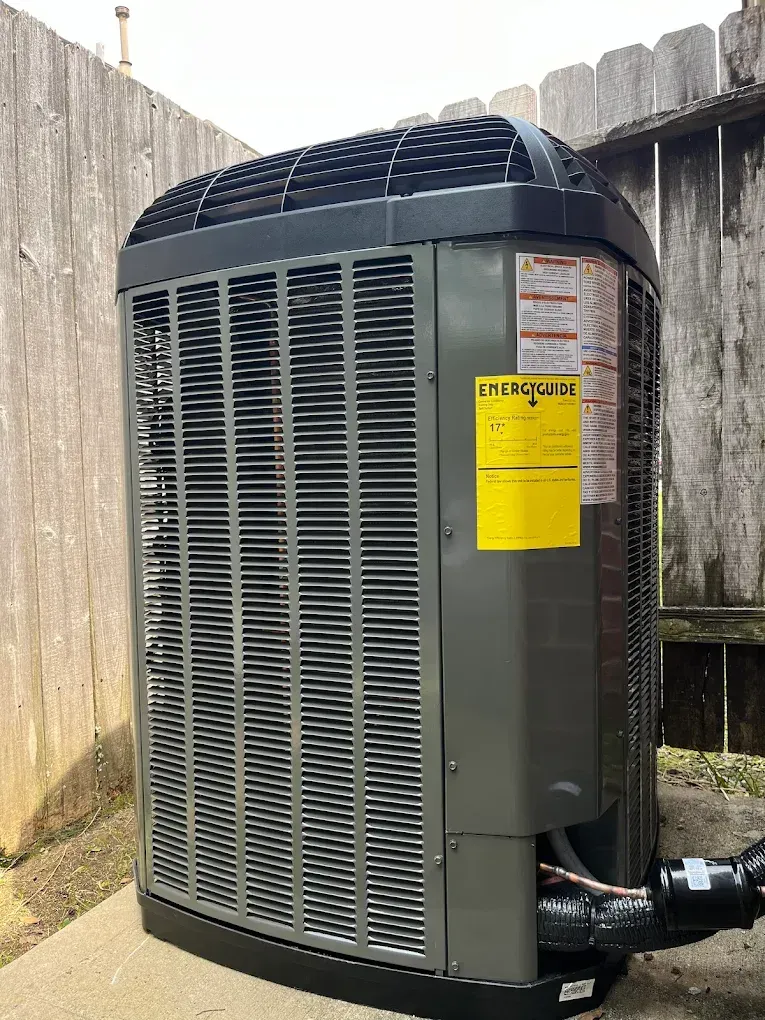 Large outdoor air conditioner unit beside a wooden fence, with yellow caution labels and attached pipes.