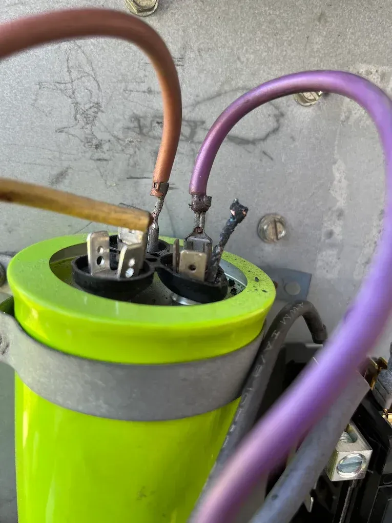 Close-up of a green cylindrical capacitor with orange and purple wires attached on a gray metal surface
