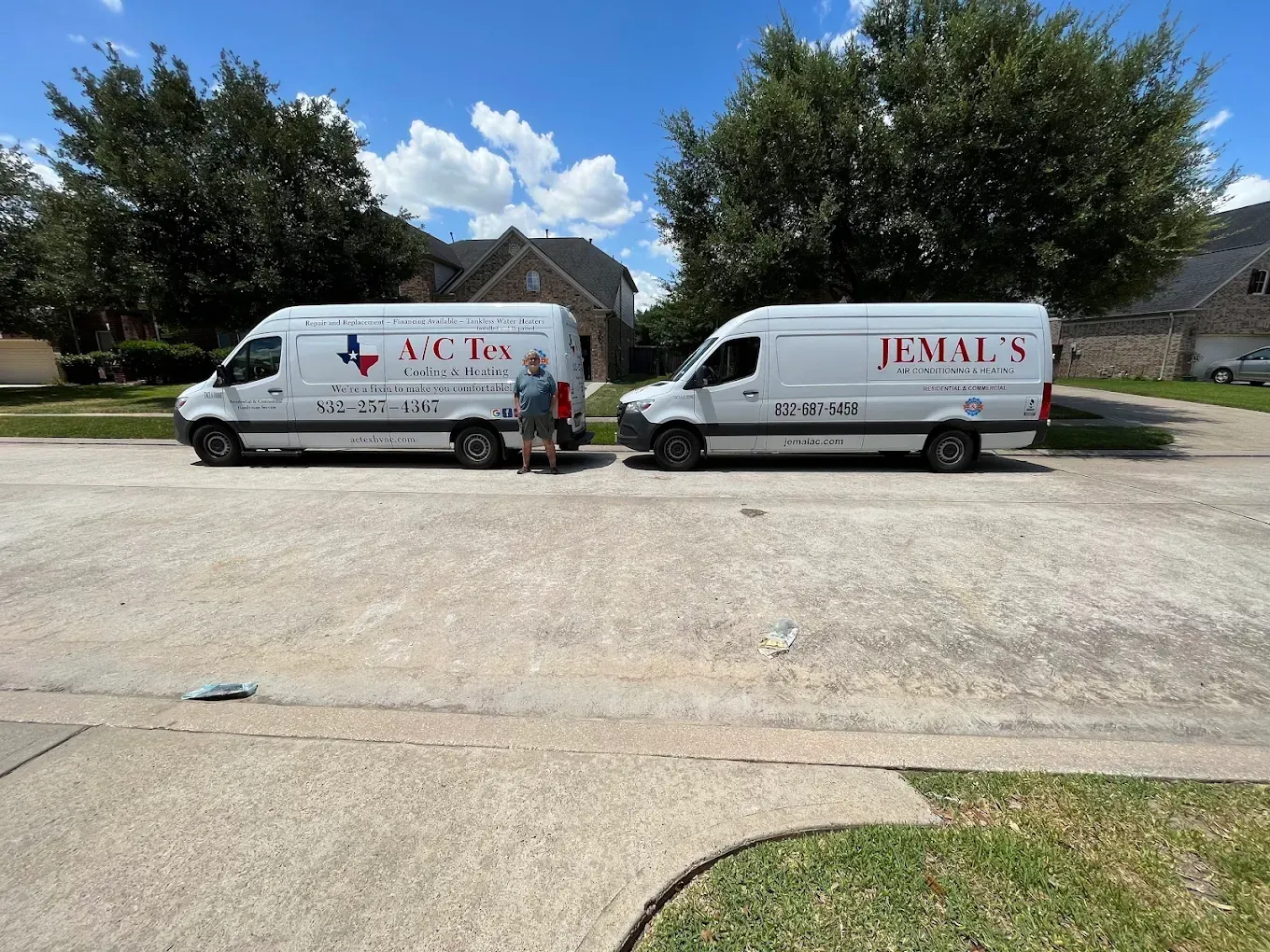 Two white service vans parked in a residential driveway, with one person standing between them.