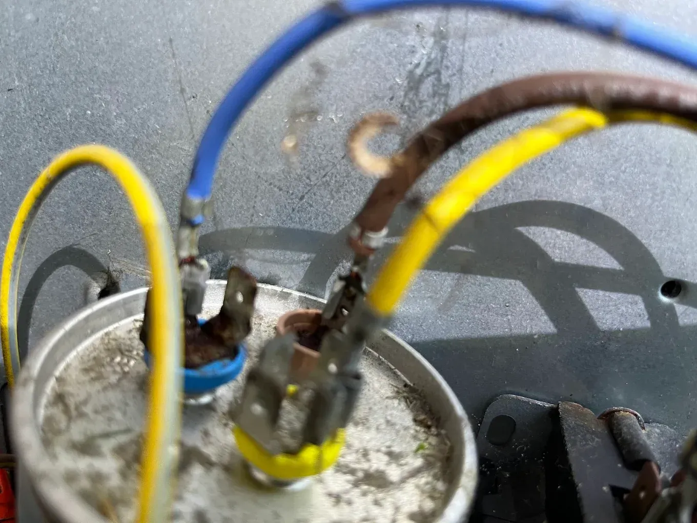 Close-up of tangled yellow, blue, and black wires connected to a dusty metal electrical component