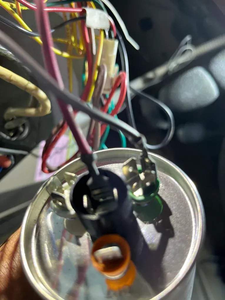 Close-up of tangled colored wires connected to a metal component with orange, black, and green terminals.