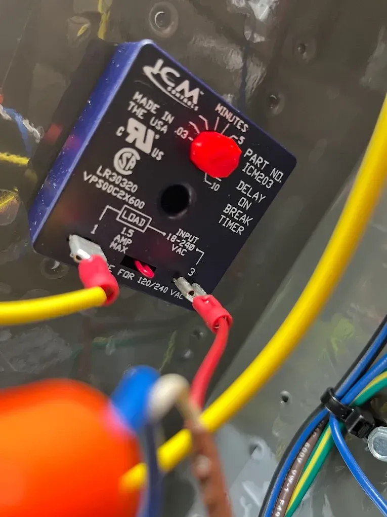 Close-up of a black electronic control panel with red knob and connected red and yellow wires inside a metal enclosure