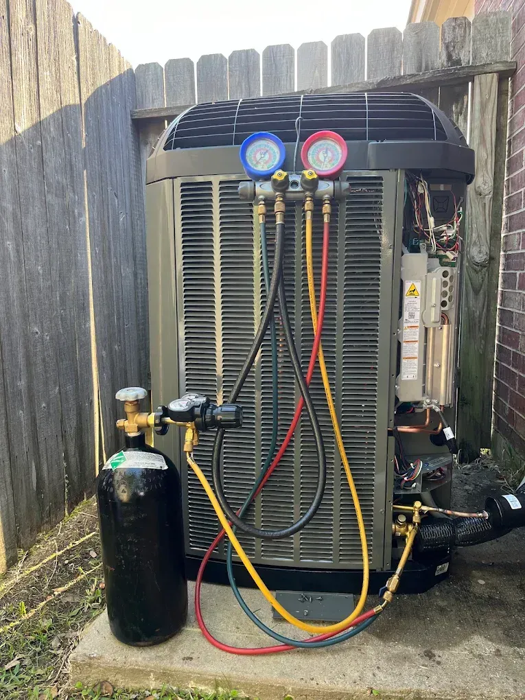 HVAC service gauges and hoses connected to an outdoor air conditioner unit beside a wooden fence.