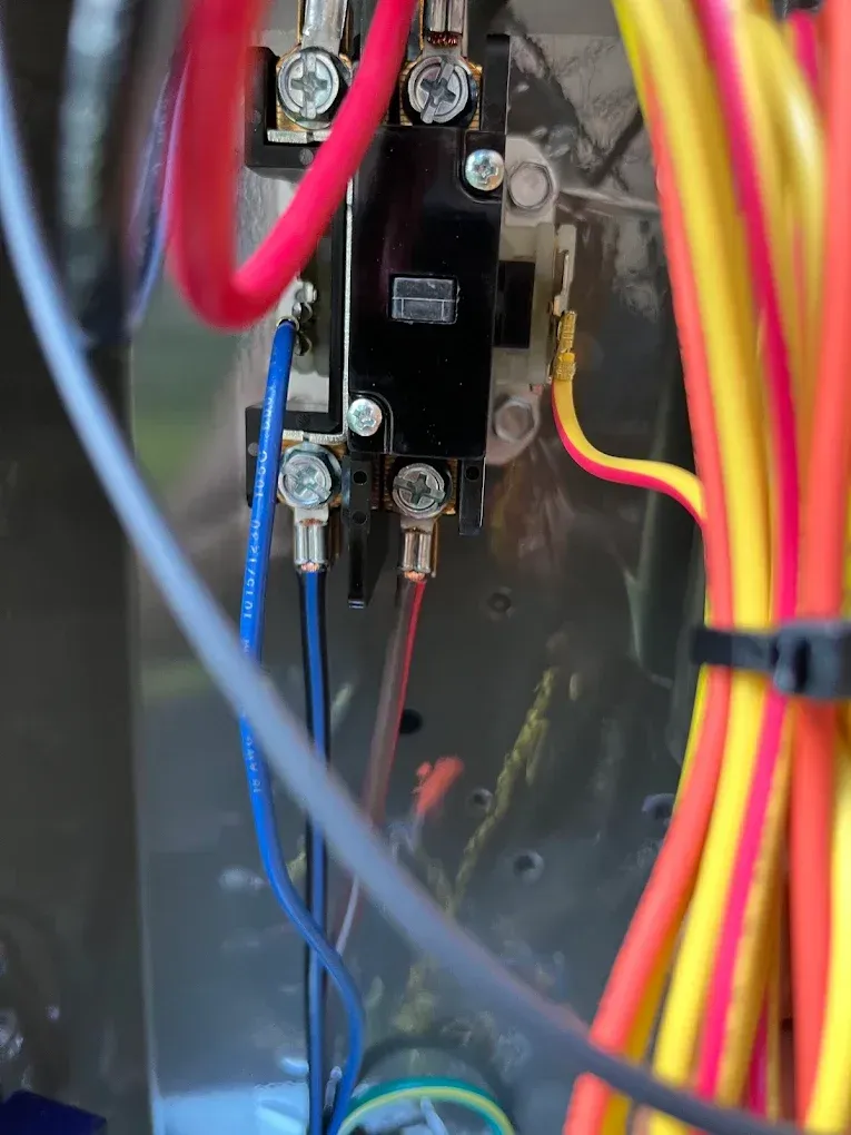 Close-up of electrical wiring and a black switch mounted inside a metal panel.