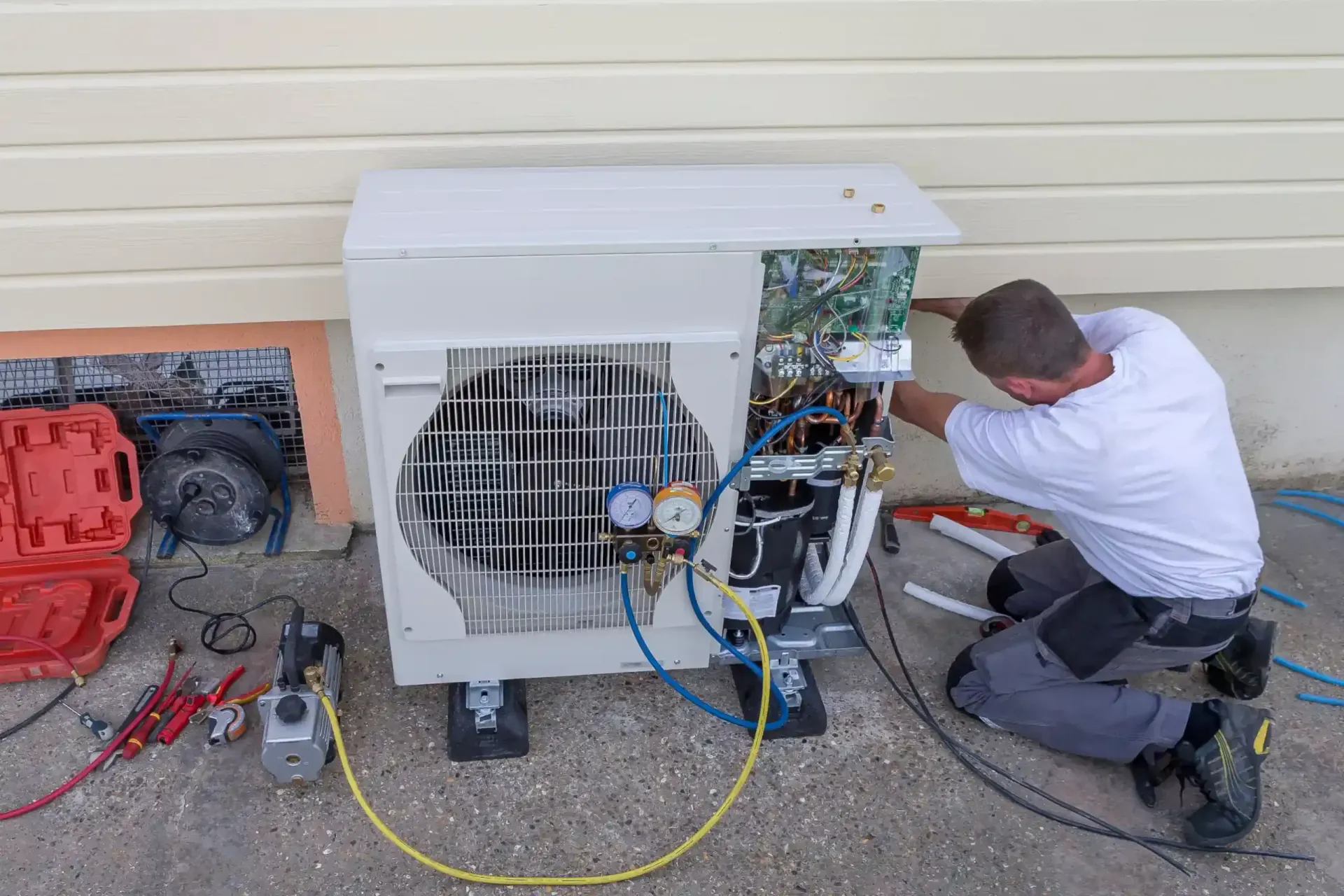 Technician kneels beside a portable HVAC unit, repairing wiring and components outdoors.
