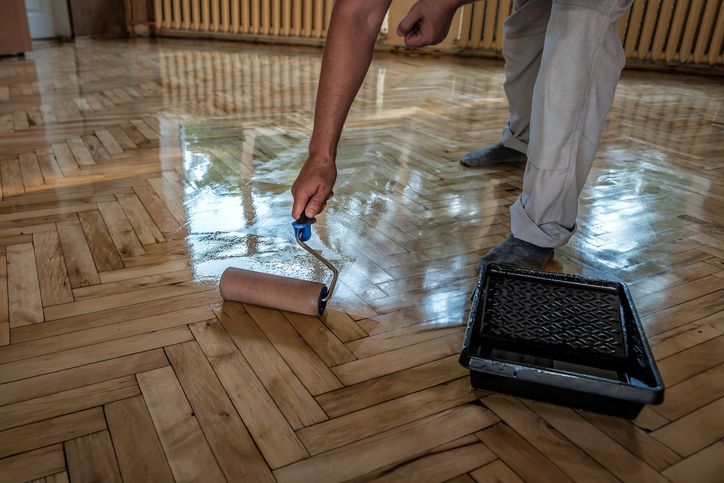 Lacquering wood floors. Worker uses a roller to coating floors