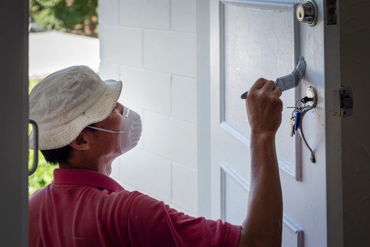 Man wearing facemask, painting a white door with paintbrush