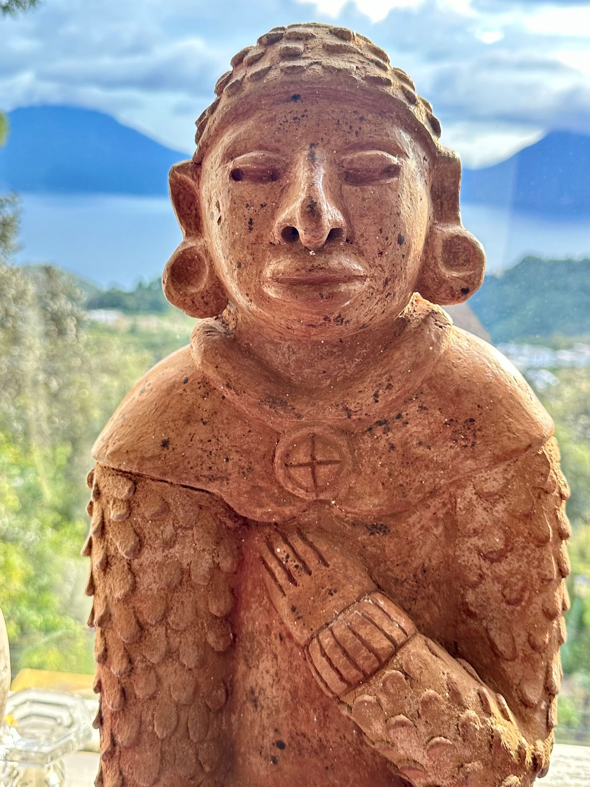Tonstatue einer Person mit geschlossenen Augen, die die Hand auf die Brust legt. Im Hintergrund ein See und Berge.