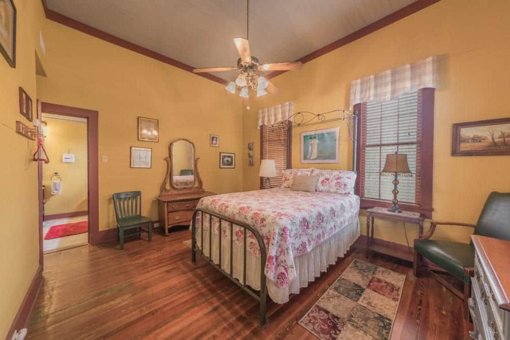 A bedroom with a bed , chair , dresser , mirror and ceiling fan.