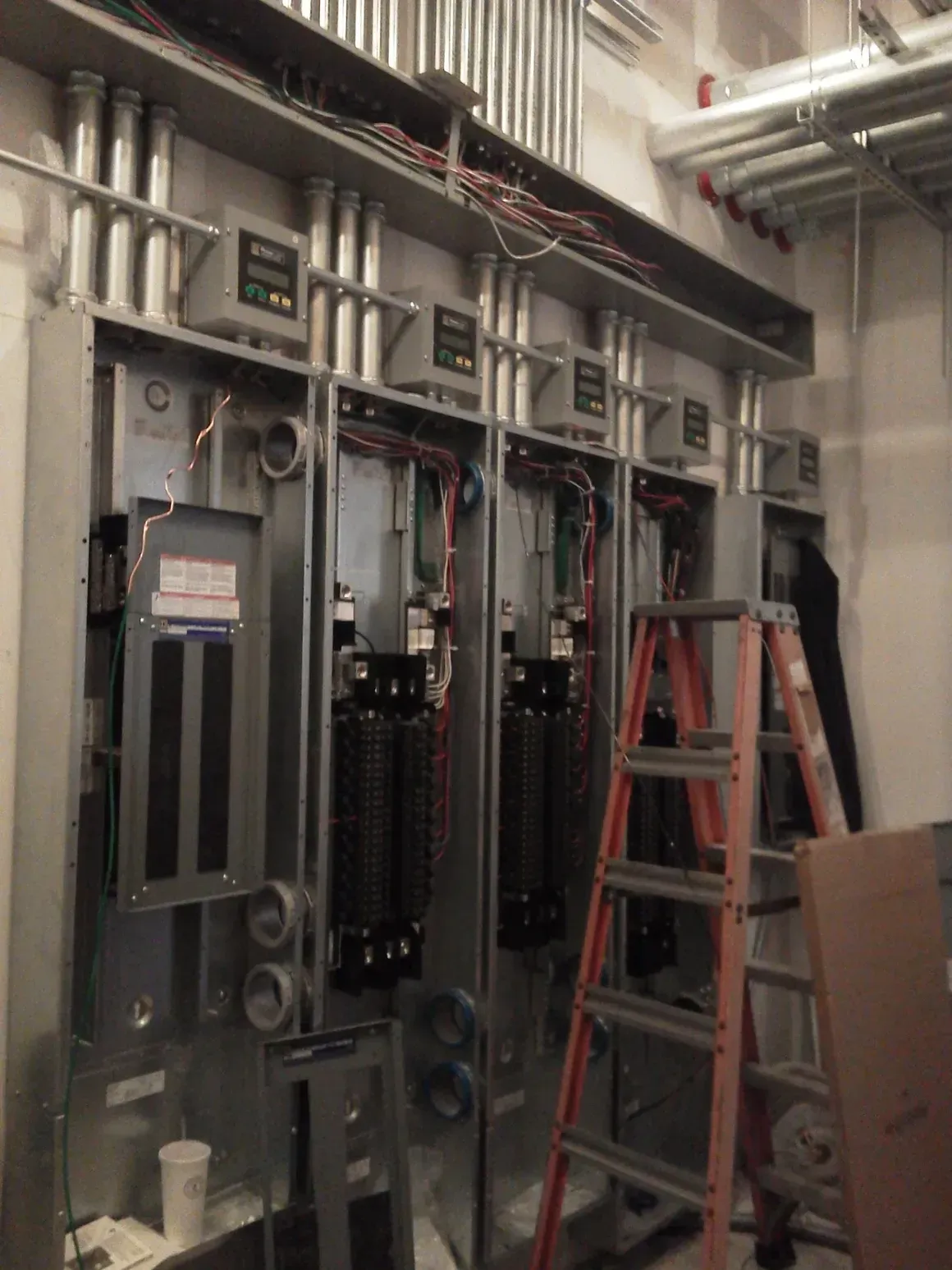 A ladder is sitting in front of a wall of electrical equipment