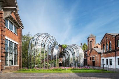 Arched metal garden sculpture between brick buildings under a blue sky