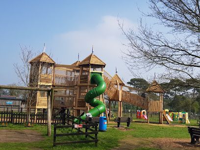 Playground with a tall green spiral slide and wooden climbing structures under a clear sky.