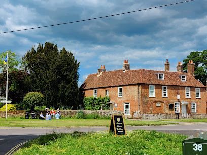 Red-brick country pub beside a road under a cloudy sky, with people sitting on benches nearby.