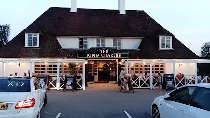 Exterior of King Charles pub at dusk, with parked cars and lit entrance signs