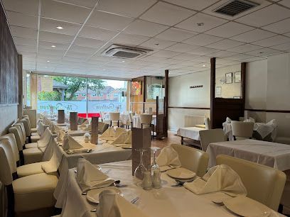 Empty elegant restaurant dining room with white tablecloths and folded napkins, lit by daylight from a front window
