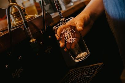 Hand holding a glass at a dimly lit bar beside beer taps