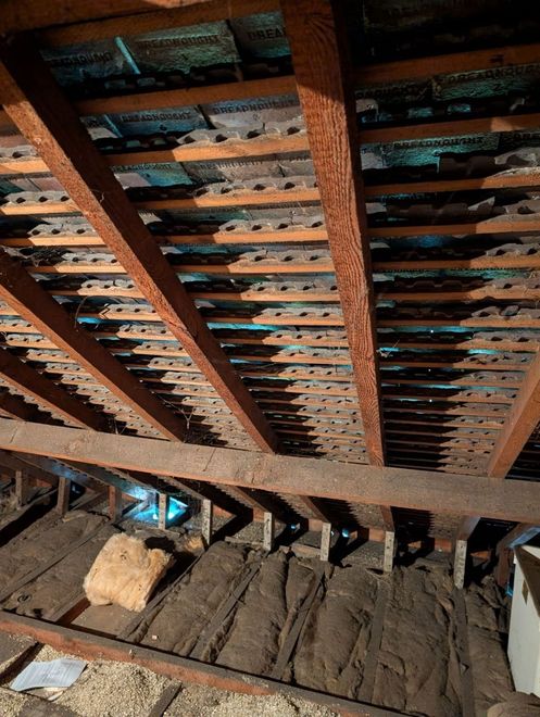 Interior roof framing with exposed wooden beams and tiles, viewed from below.