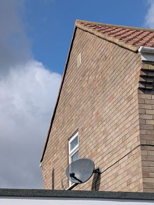 Brick house exterior with red tiled roof, small window, and a satellite dish against a blue sky