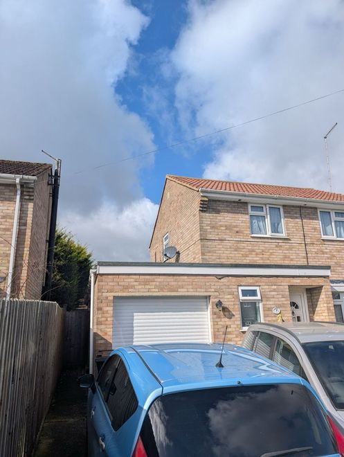 Brick houses and a garage under a cloudy sky, with parked cars in the foreground