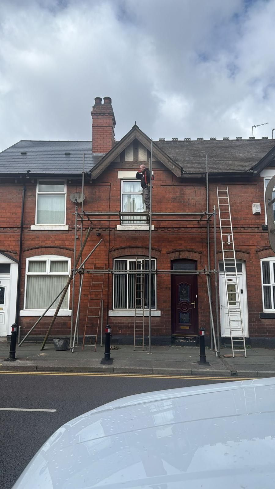 Brick terraced house front with scaffolding, white-framed windows, and a cloudy sky above