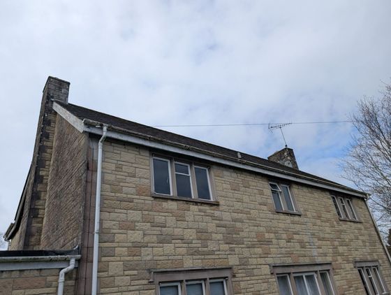 Stone house exterior with pitched roof and chimney against a cloudy sky
