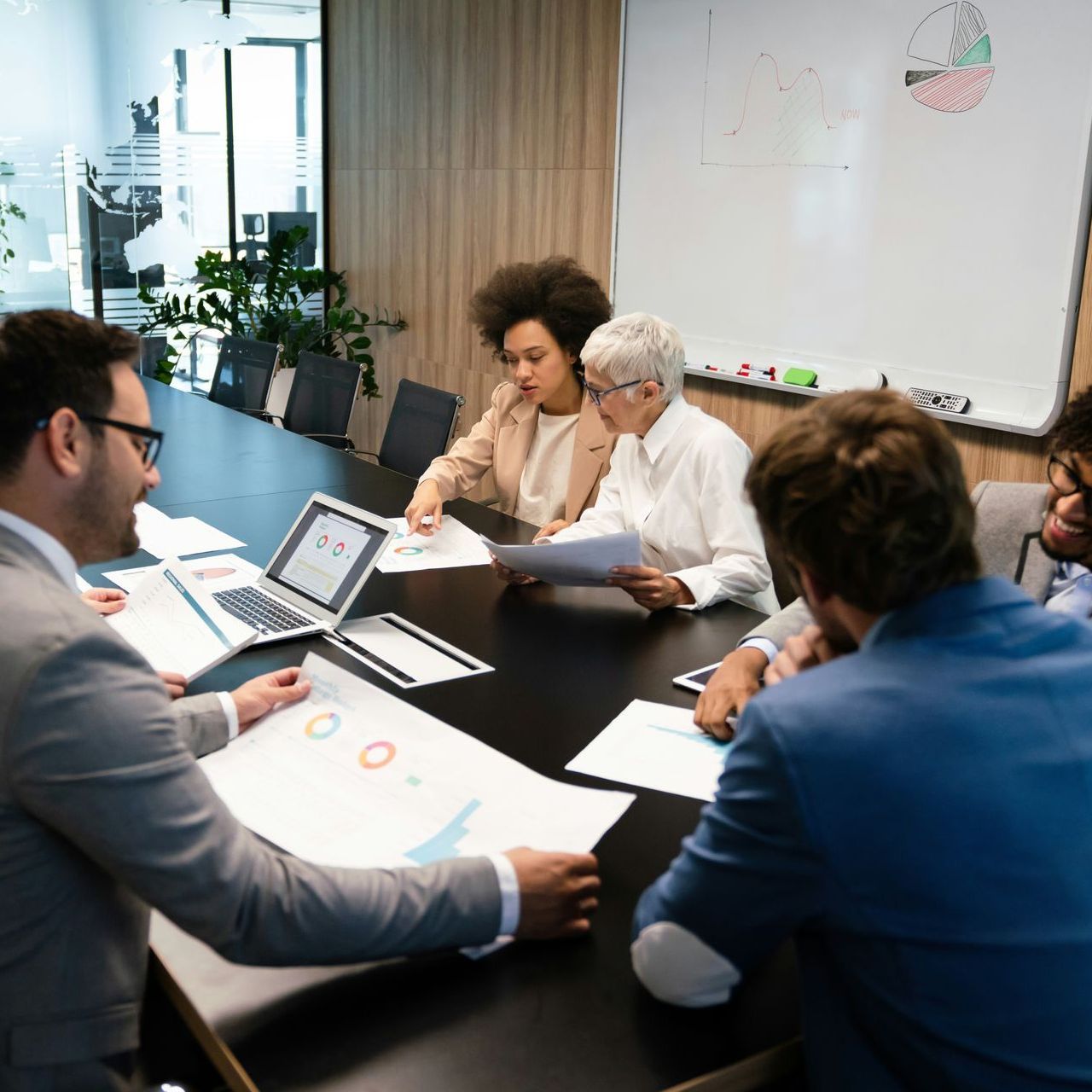 Business meeting: People at a table, looking at documents and a laptop. Various skin tones.