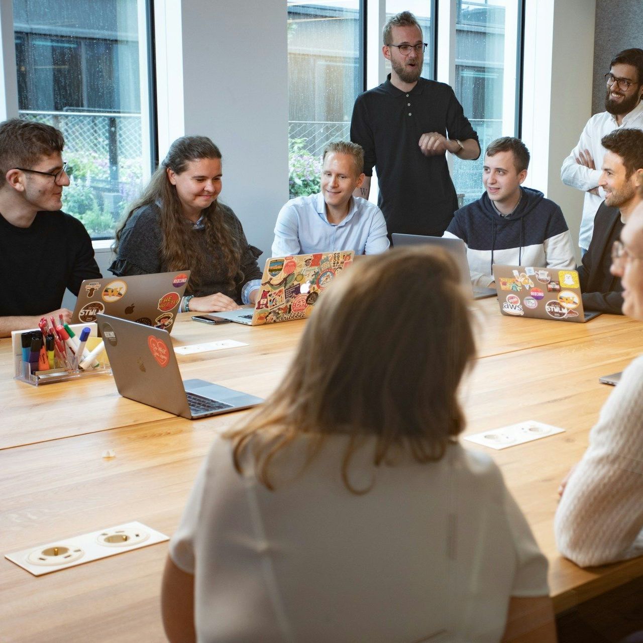 Group of people in a meeting at a long wooden table, discussing ideas in a modern office setting.