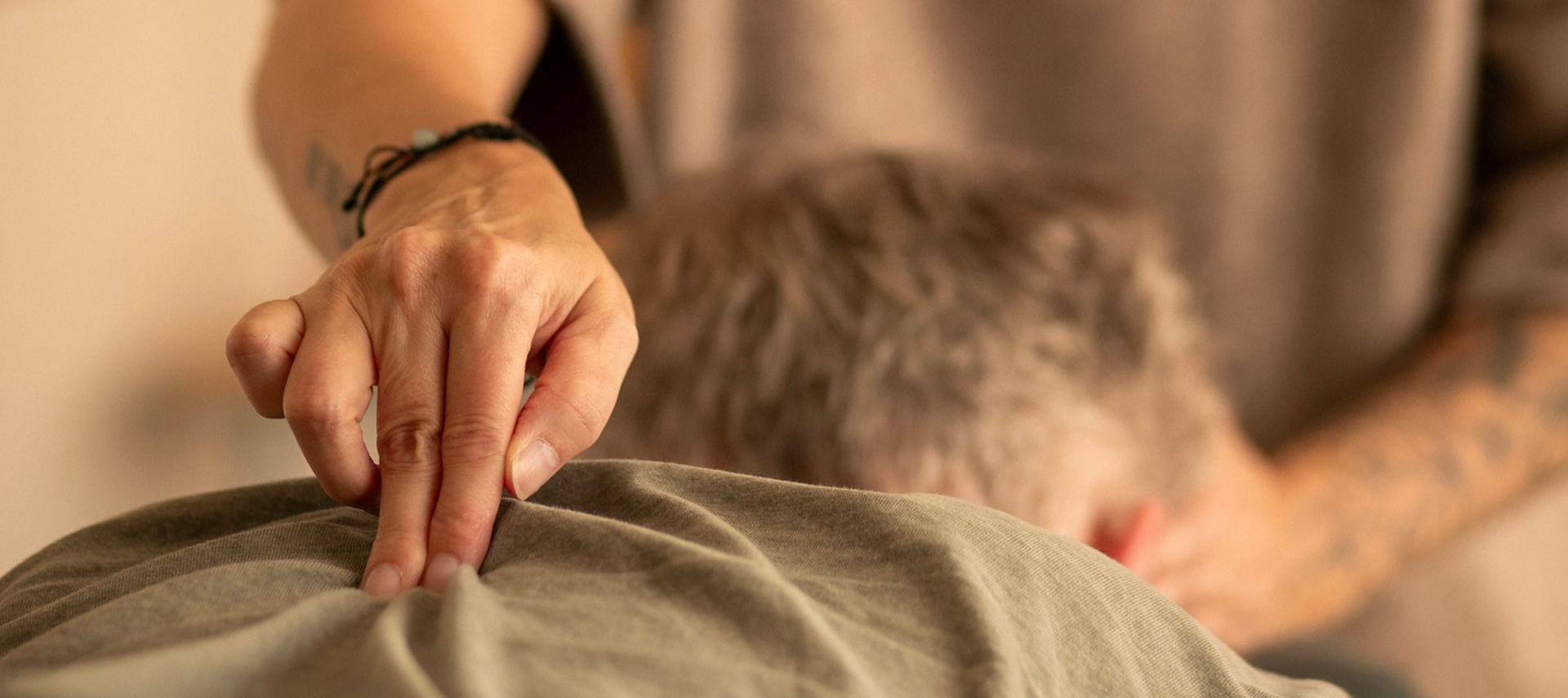 Handen geven een schoudermassage aan een zittende persoon in een warme, zacht verlichte kamer.