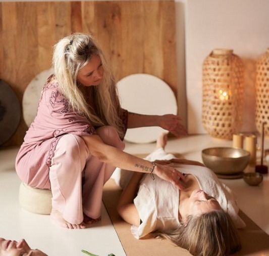 Vrouw in roze verzorgt een andere vrouw die op de grond ligt in een rustige ruimte.