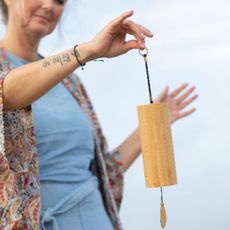 Een persoon houdt buiten een houten, pendelachtig voorwerp, Koshi shime, vast tegen een wazige hemel.