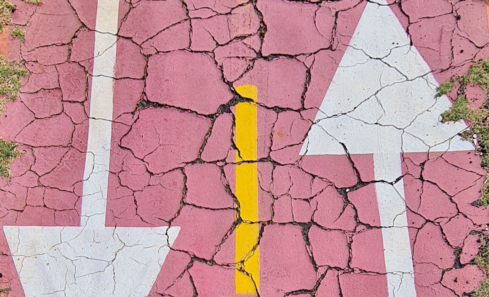 Gebarsten roze bestrating met witte pijlen en een gele middenlijn die een gemarkeerde weg of pad aangeeft.