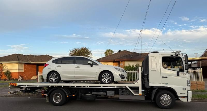 Tow truck carrying a white SUV on a flatbed in a suburban street