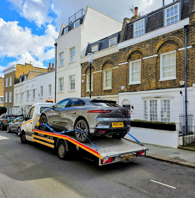 Silver sports car on a tow truck parked on a residential street with white and brick townhouses.