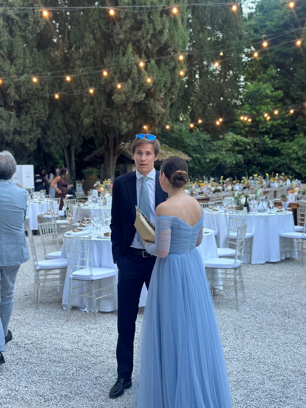 Couple dancing at an outdoor evening reception with string lights and round white tables